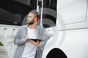 Young handsome truck driver is standing with a tablet near the truck