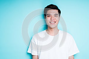 Young handsome vietnamese man in t-shirt smiling broadly while standing against blue background