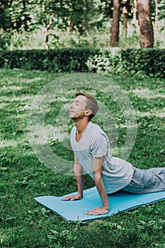 Young handsome white man in sportswear does stretching in the park on the green grass.