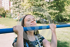 A young handsome woman in casual clothes is doing pull up exercise on horizontal bar. fitness, sport, exercising