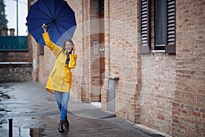 A young handsome woman in a yellow raincoat and with umbrella is having a phone call while walking the city on a rainy day. Walk,