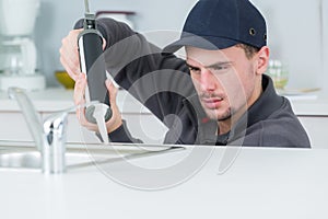 Young handyman applying silicone sealant with gun around sink