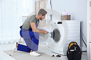 Young handyman fixing washing machine at home.