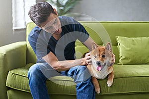Young hansome man in t-shirt playing and stroking his lovely Shiba Inu dog
