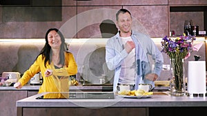 Young happy active family couple dancing laughing together preparing food at home, carefree joyful husband and wife having fun