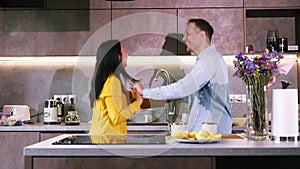 Young happy active family couple dancing laughing together preparing food at home, carefree joyful husband and wife having fun