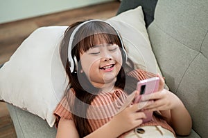 Young happy and adorable Asian girl is using a smartphone while lying on a sofa in the living room