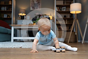 Young happy adorable baby girl or boy sitting on the floor of apartment playing with his or her favorite toy. Cute child crawling