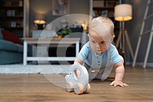 Young happy adorable baby girl or boy sitting on the floor of apartment playing with his or her favorite toy. Cute child crawling