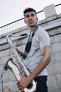 Young and happy african american street musician holding saxophone