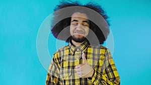Young happy afro american man smiling while giving thumbs up on Blue background. Concept of emotions