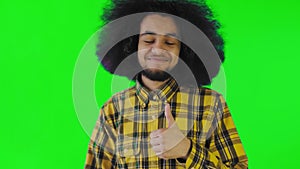 Young happy afro american man smiling while giving thumbs up on green screen or chroma key background. Concept of