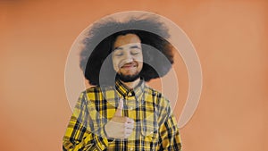 Young happy afro american man smiling while giving thumbs up on Orange background. Concept of emotions