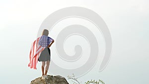 Young happy american woman with long hair raising up waving on wind USA national flag in her hands relaxing outdoors enjoying warm