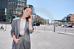 Young happy Asian business woman entrepreneur talking on phone on city street.