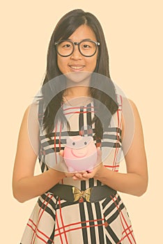 Young happy Asian businesswoman holding piggy bank