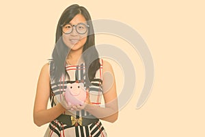 Young happy Asian businesswoman holding piggy bank
