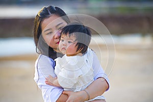 Young happy Asian Chinese woman mother of adorable baby girl holding her sweet little daughter in her arms taking a walk at