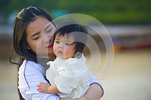 Young happy Asian Chinese woman mother of adorable baby girl holding her sweet little daughter in her arms taking a walk at