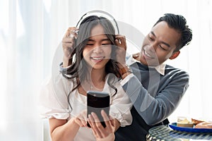 Young happy Asian couple enjoying listening to music together, spending time together at home