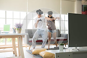 Young happy Asian couple playing video games wearing virtual reality glasses in their apartment