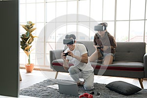 Young happy Asian couple playing video games wearing virtual reality glasses in their apartment