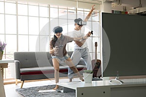 Young happy Asian couple playing video games wearing virtual reality glasses in their apartment