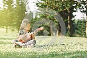 Young and happy asian girl playing with ukelele guitar at the park in sunny morning