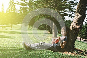 Young and happy asian girl playing with ukelele guitar at the park in sunny morning