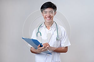 Young happy Asian medical doctor holding medical chart over gray studio background