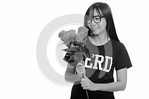 Young happy Asian nerd teenage girl smiling and holding red roses ready for Valentine`s day