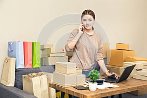 Young happy asian online seller, business woman, in her home talking to her customer on her phone while looking at camera