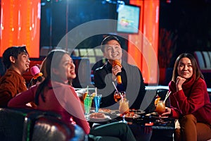 Young happy asian people having fun while singing karaoke on night party at bar.