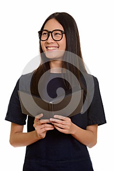 Young happy Asian teenage girl smiling while holding book and th