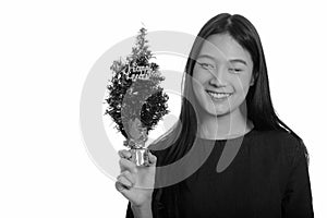 Young happy Asian teenage girl smiling and holding Happy New Year tree