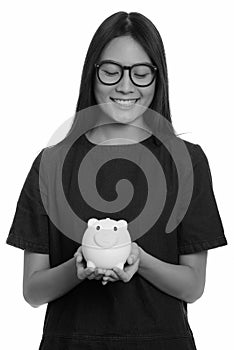 Young happy Asian teenage girl smiling and holding piggy bank