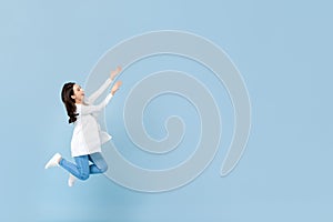 Young happy Asian woman floating in mid-air with hands opening to blank space beside in blue isolated