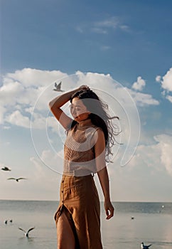 Happy asian woman with hands in the air walks on the seaside in autumn. Seagulls flying on the beach.