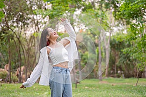 A young, happy Asian woman joyfully dances in a lush green park, expressing freedom