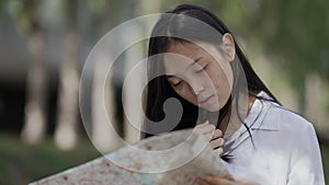 Young happy Asian woman with paper map standing on park alley choosing direction. Portrait of relaxed confident