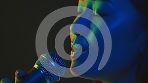 Young happy asian woman singer singing into mic in bright neon lights, nightlife and karaoke concept, profile portrait