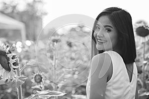 Young happy Asian woman smiling and looking back in the field of blooming sunflowers