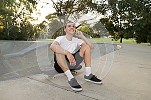 Young happy and attractive American man 30s sitting on skate board after sport boarding training session talking on mobile phone