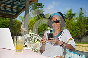 Young happy and attractive Asian American mixed ethnicity woman working with laptop computer and mobile phone from beautiful cafe