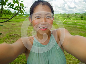 Young happy and attractive Asian Chinese woman taking selfie self portrait with mobile phone at tropical island posing cheerful