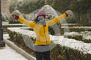 Young happy and attractive Asian Chinese woman in Winter jacket and beanie enjoying snowfall at city park playing cheerful