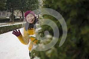 Young happy and attractive Asian Japanese woman in Winter jacket and beanie enjoying snowfall at city park playing cheerful