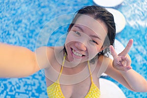 Young happy and attractive Asian Korean woman enjoying relaxed and cheerful taking selfie photo in swimming pool at hotel resort