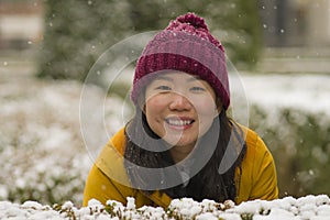 Young happy and attractive Asian Korean woman in Winter jacket and beanie enjoying snowfall at city park playing cheerful
