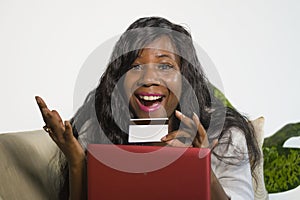 Young happy and attractive black African American woman using credit card and laptop computer banking online and shopping on inter